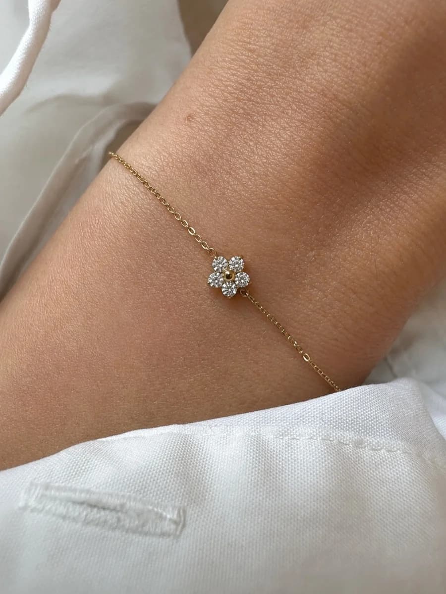 A fine gold-tone chain bracelet with a crystal-set flower charm, worn on a wrist against white linen.