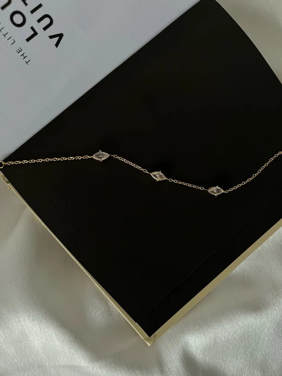A slim gold-tone chain bracelet with crystal-set charms, resting on a black book cover.
