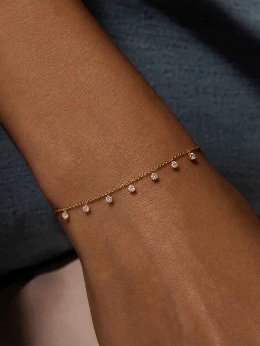 Close-up of a person's wrist wearing a gold-tone chain bracelet with seven small, sparkling crystal drop charms.