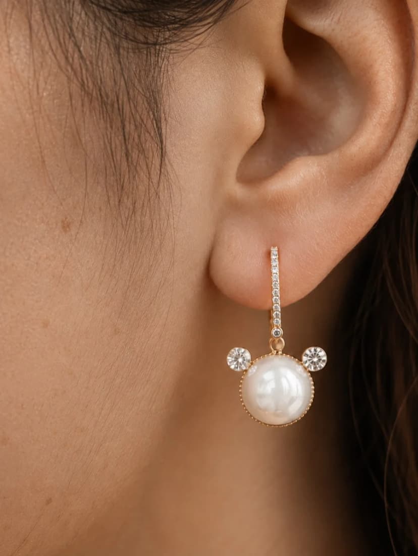 Close-up of a person's earlobe wearing a gold-tone drop earring with a large pearl-like bead and two smaller crystal-set circles.