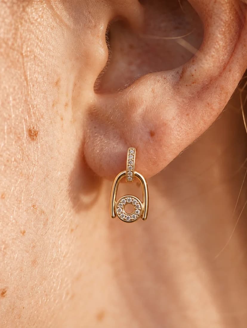 Close-up of a person's earlobe wearing a gold-tone drop earring with a crystal-set post and an open circle charm.