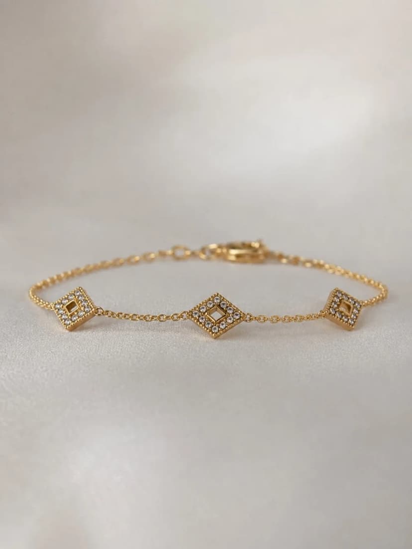 A gold-tone chain bracelet with three rhombus-shaped charms, each sparkling with tiny crystals. The bracelet is laid flat on a light background.
