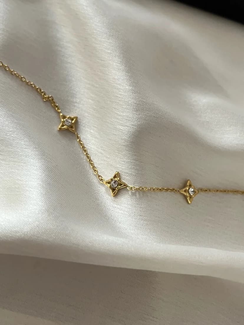 A gold-tone chain bracelet with four small crystal-centred star charms is laid on a white satin fabric.