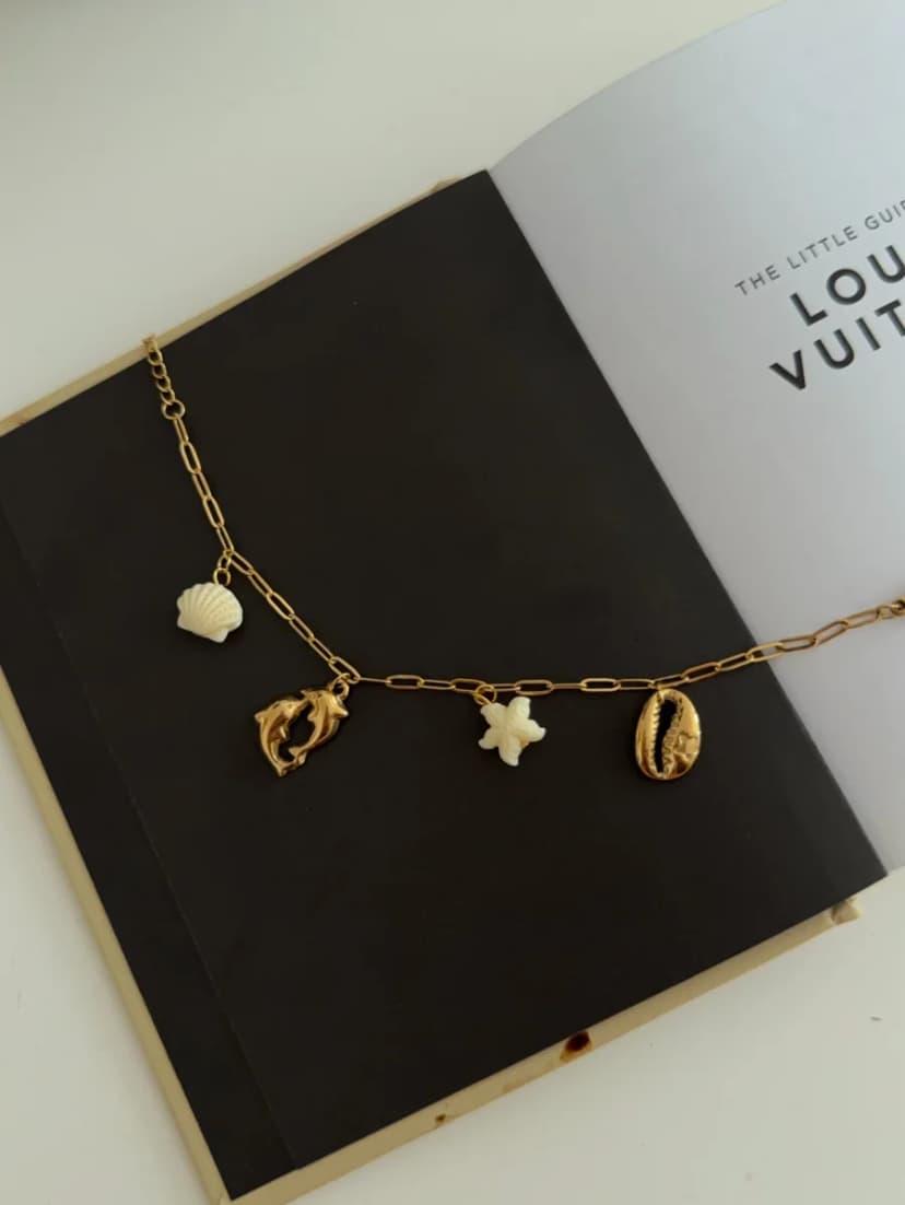 A gold-tone chain bracelet with shell, dolphin, and starfish charms rests on an open black book.