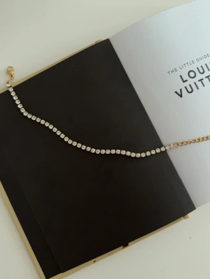 A delicate bracelet with a long section of tiny clear crystals and a fine gold-tone chain with a clasp, lying on an open book.