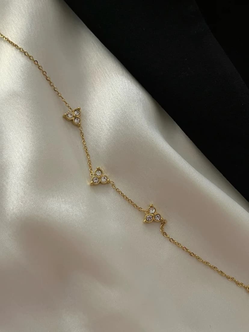 A delicate gold-tone chain bracelet with three crystal-set triangular motifs lies on white satin fabric.