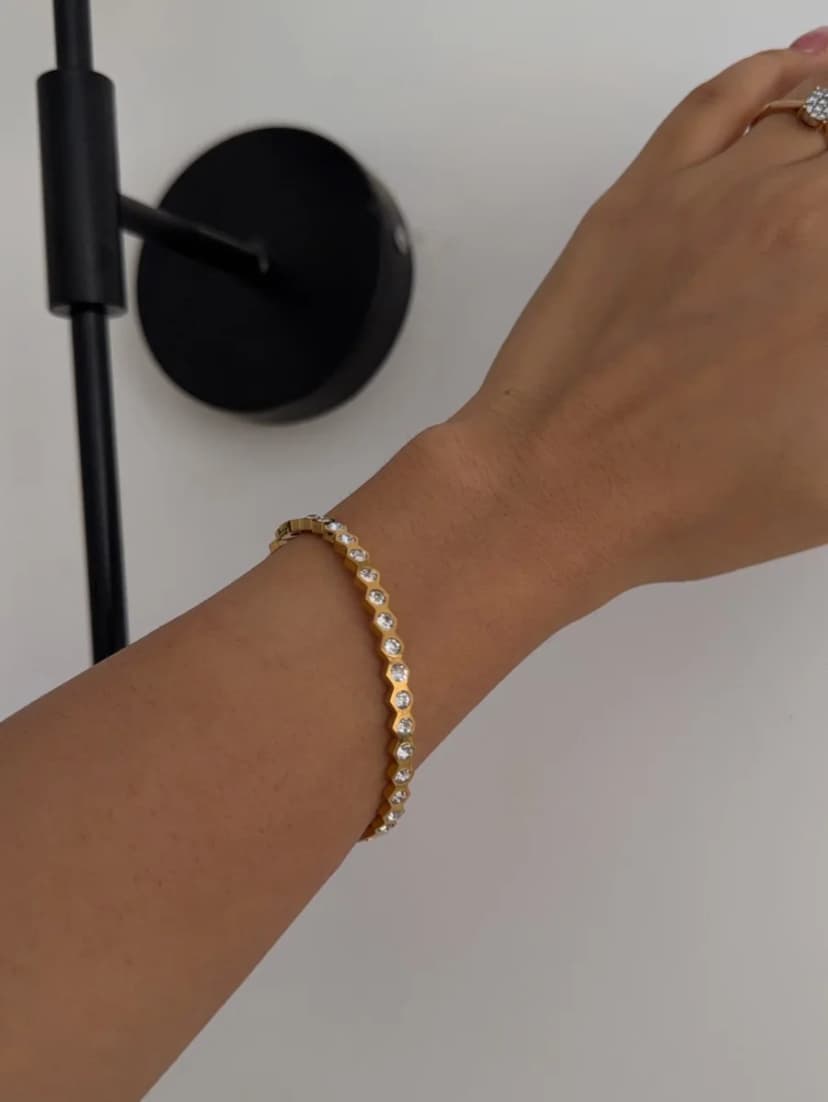 A gold-tone bracelet with a hexagonal pattern and clear crystals is worn on a light-skinned arm.