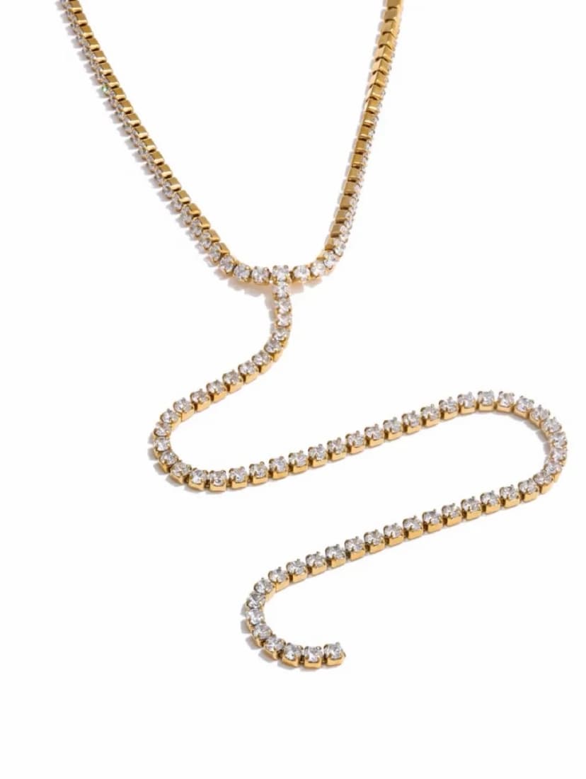 A gold-tone lariat necklace with clear crystal-like stones, forming a Y-shape with a long, wavy drop on a white background.