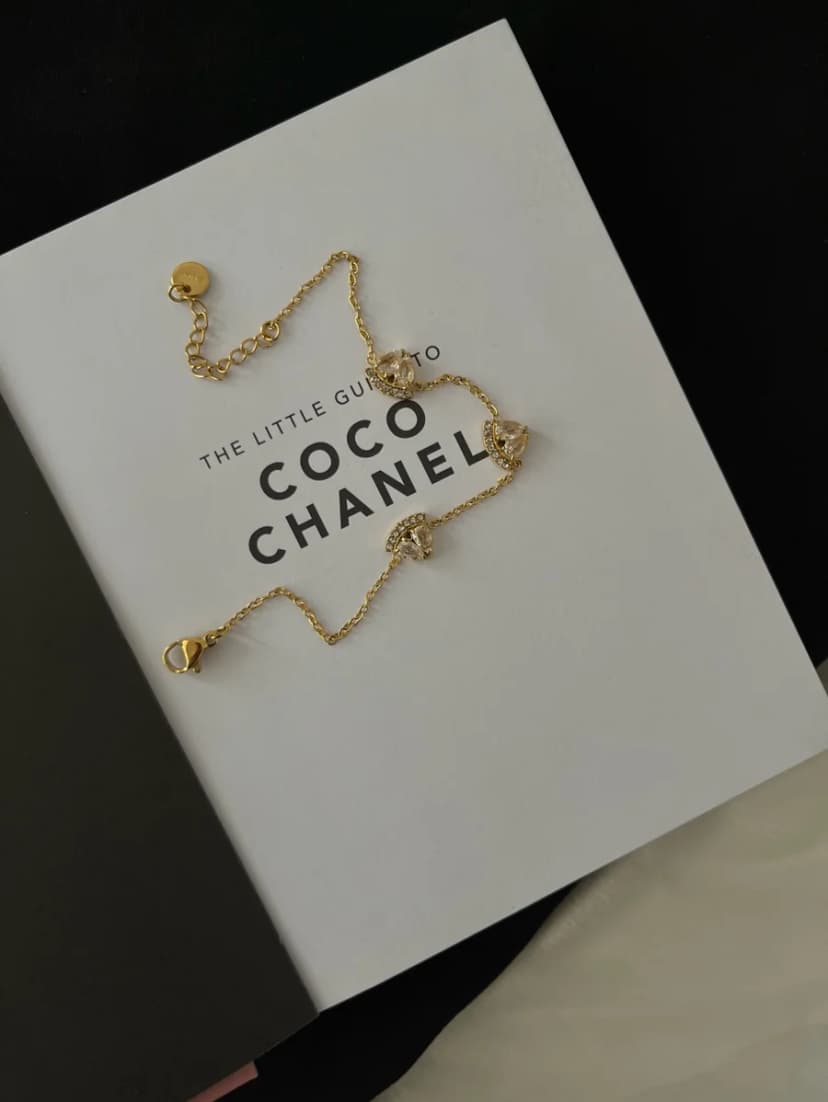 A delicate gold-tone chain bracelet with three sparkling, clear crystal-set charms, displayed on an open white book.