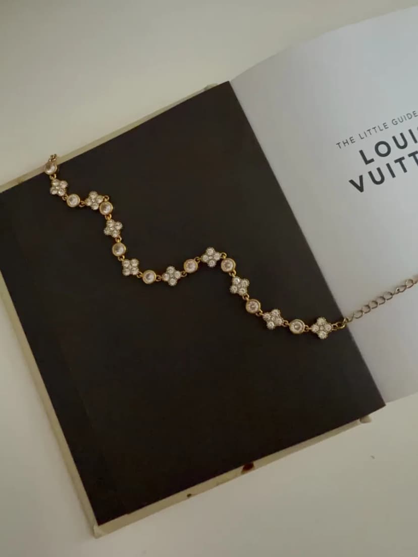 A wavy gold-tone bracelet with alternating crystal-set flowers and round crystals, laid on an open book.