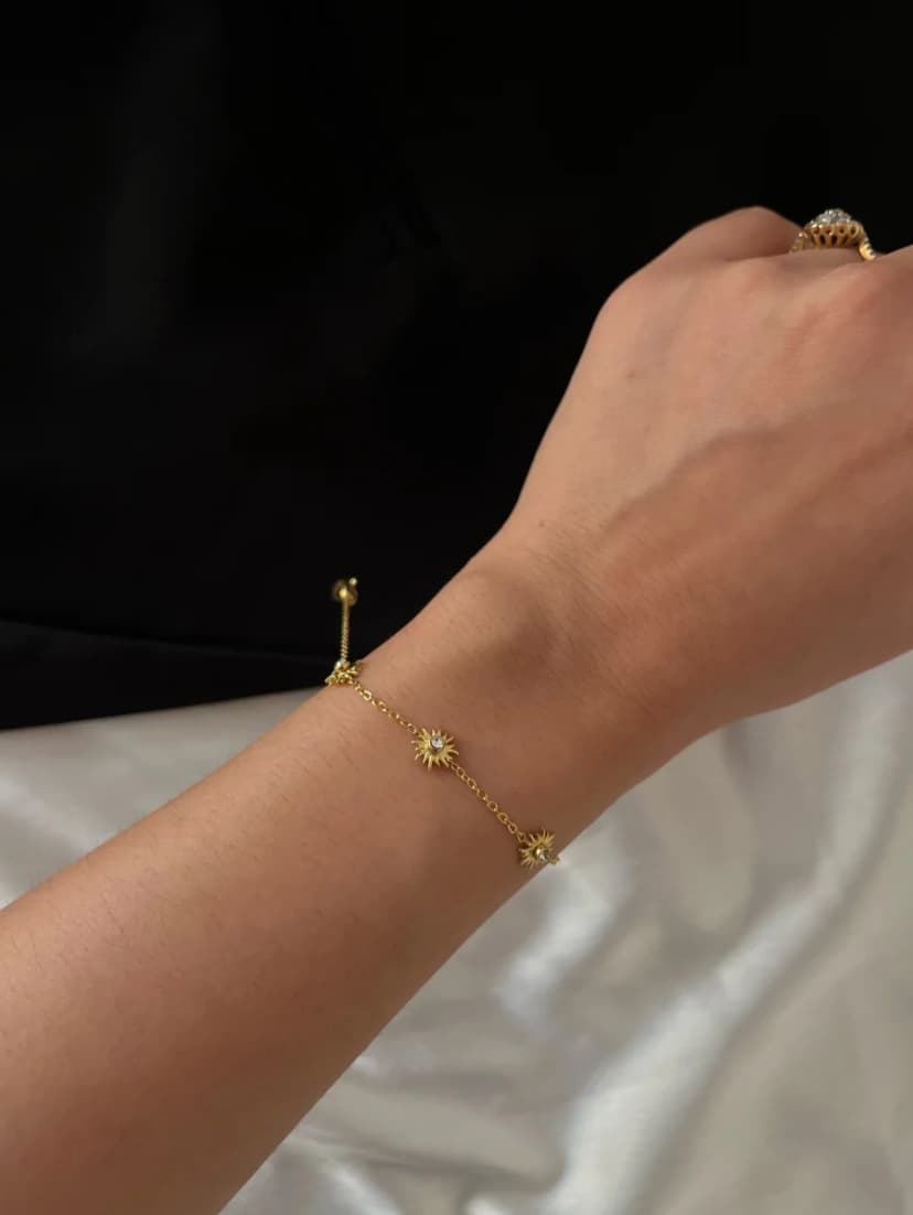 A person's arm wearing a delicate gold-tone chain bracelet with three small crystal-set star charms.