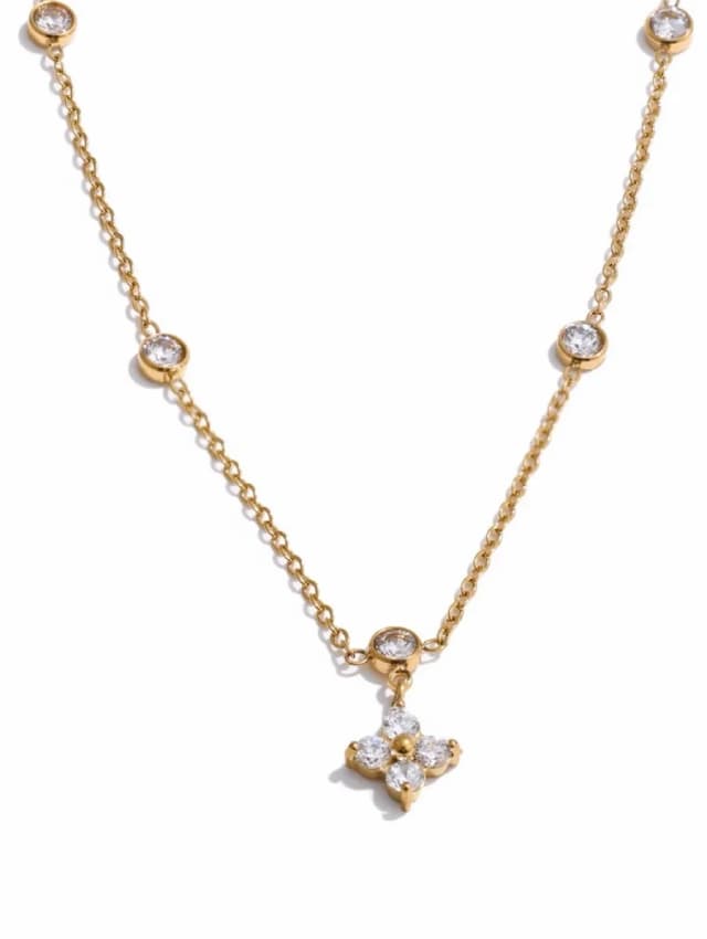 A gold-tone necklace with a central crystal-set flower charm and several round crystal stations on a white background.