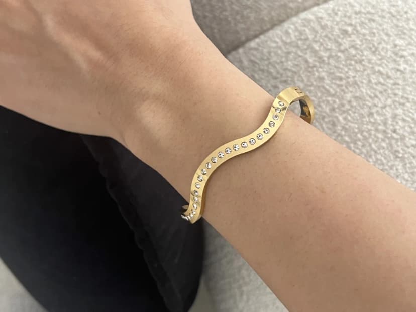 A person's arm wearing a gold-tone wavy cuff bracelet completely covered in small clear crystals.