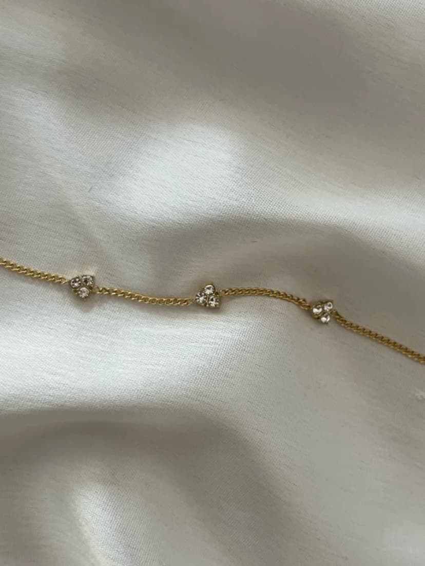 A gold-tone chain bracelet with three small, spaced crystal-set flower motifs, lying on a white wrinkled fabric.